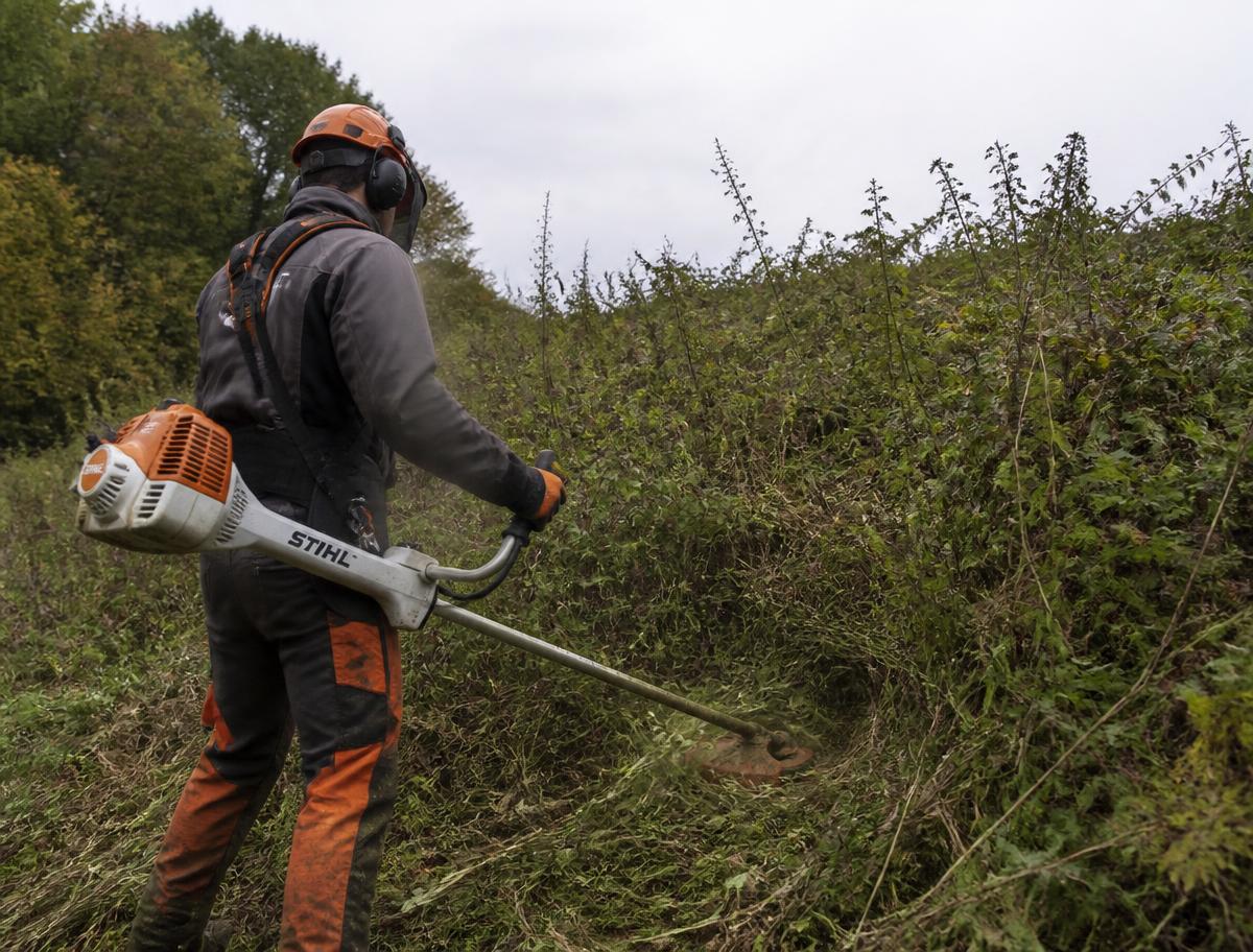 Ouvrier débroussaillant un talus couvert de ronces à la débroussailleuse