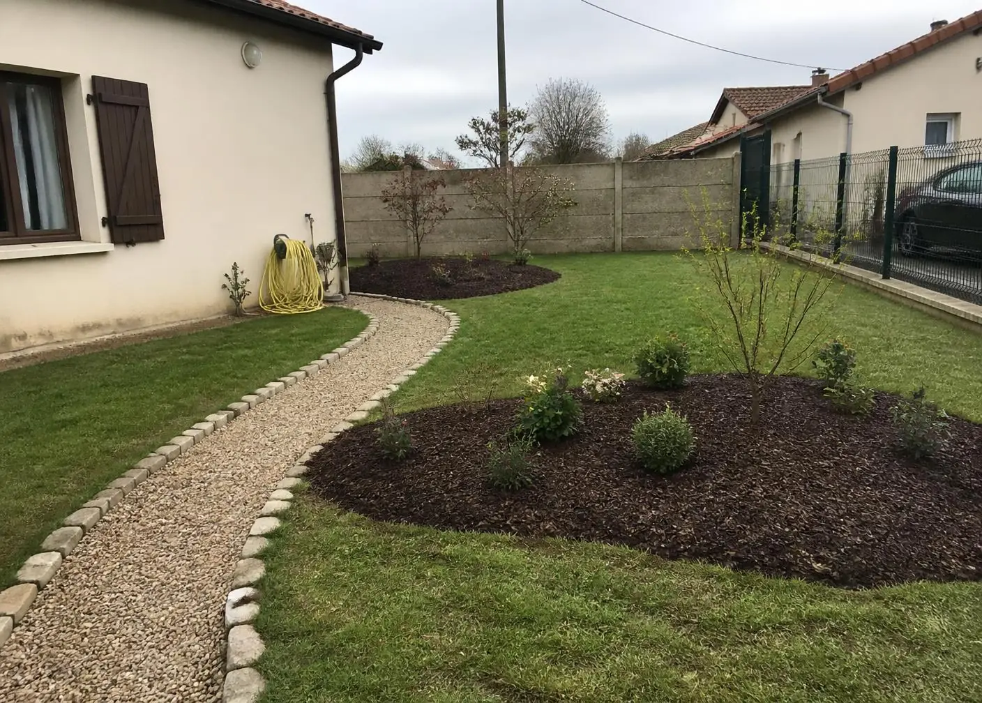 Jardin aménagé : pelouse, allée de gravier bordée de pavés et massifs paillés plantés de jeunes arbustes