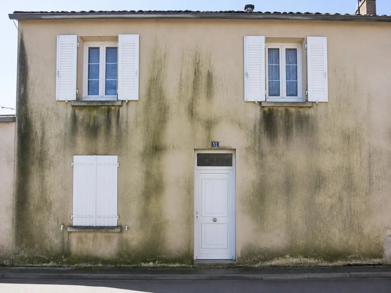 Façade crépie striée de coulures vertes et noires sous les fenêtres