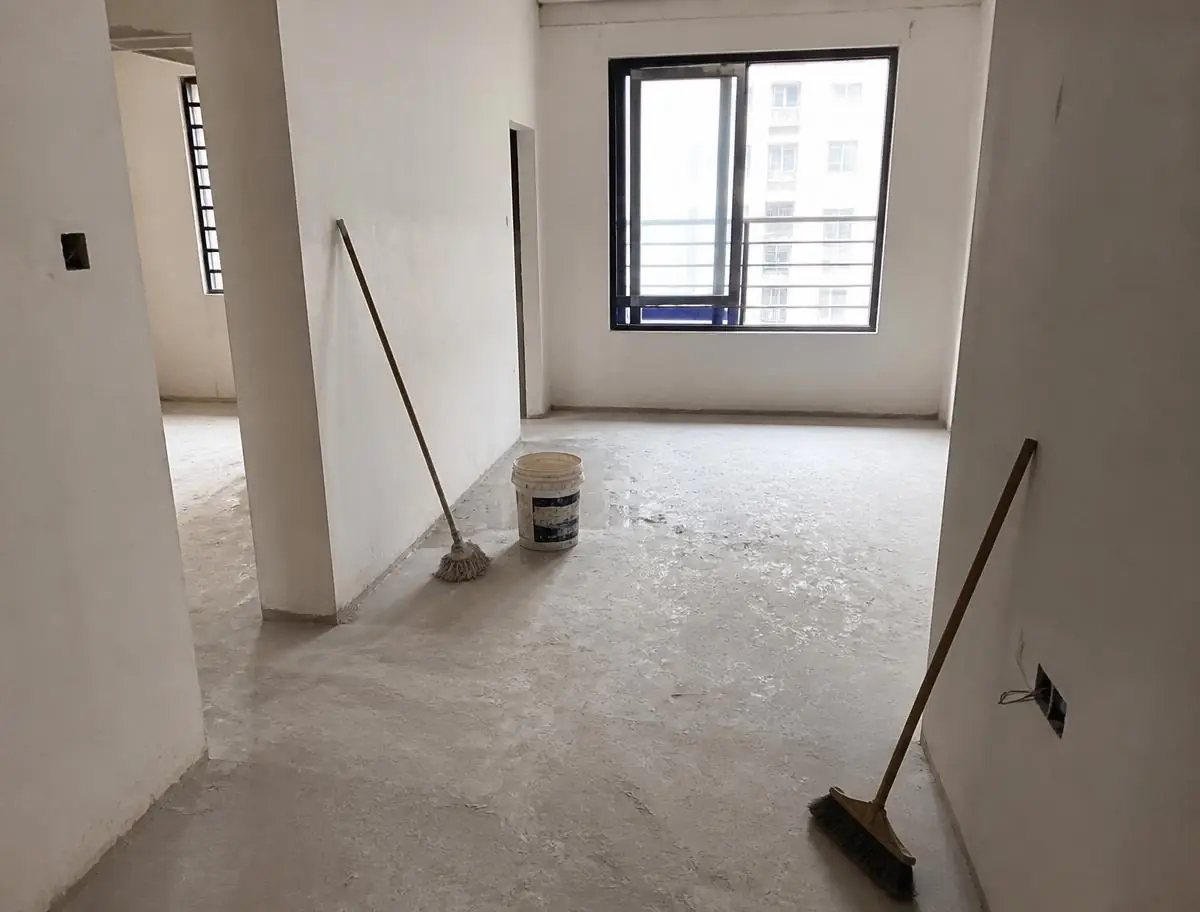 Appartement neuf et vide après travaux, sol poussiéreux, seau, balai et serpillière posés dans la pièce