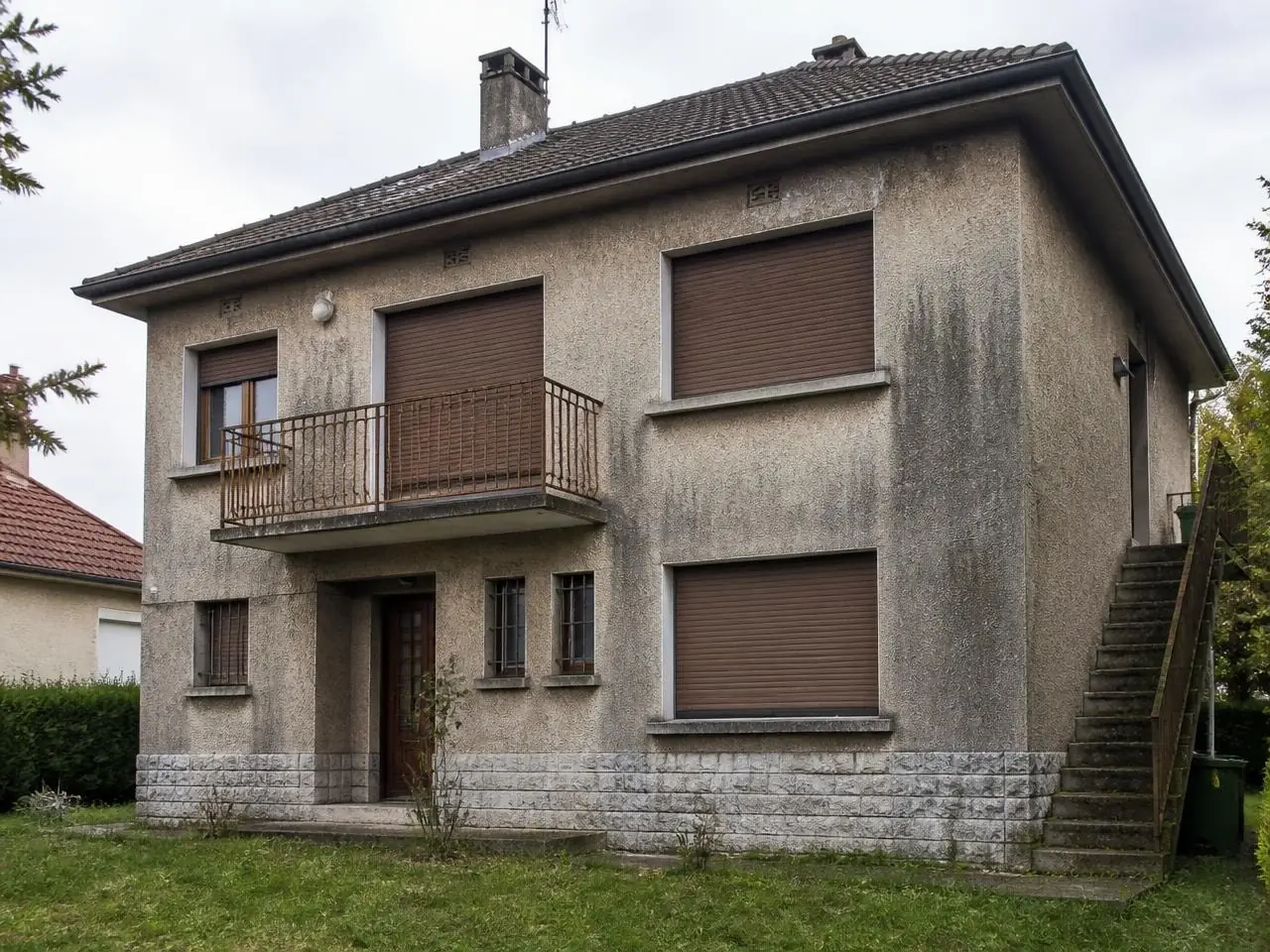 Maison à l’enduit gris marquée de longues coulures sombres sous le toit et sous les fenêtres
