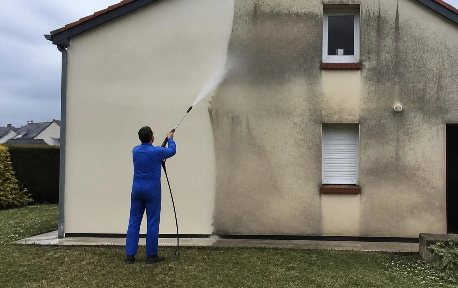 Pignon de maison lavé au jet haute pression : la partie gauche déjà claire, la partie droite encore noircie