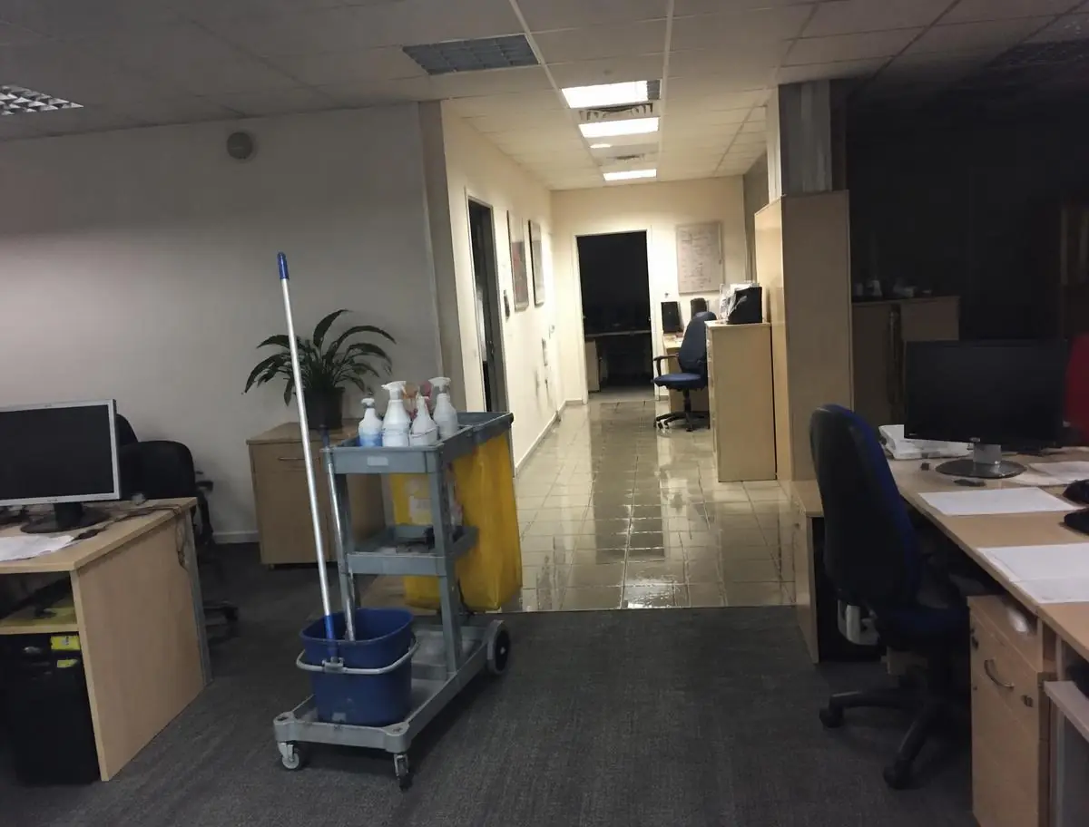 Chariot de ménage devant un couloir de bureaux au carrelage fraîchement lavé